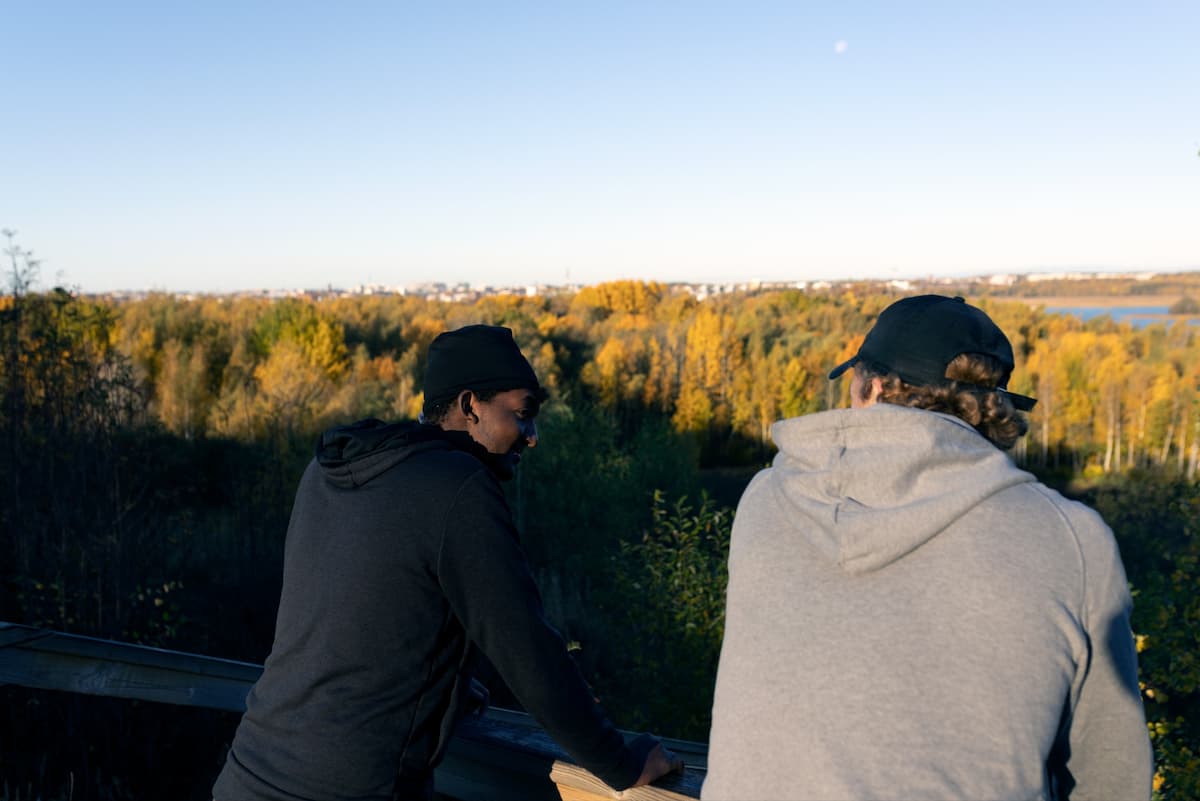 Kaksi nuorta henkilöä istuu korkealla mäellä, josta avautuu näkymä Helsinkiin.