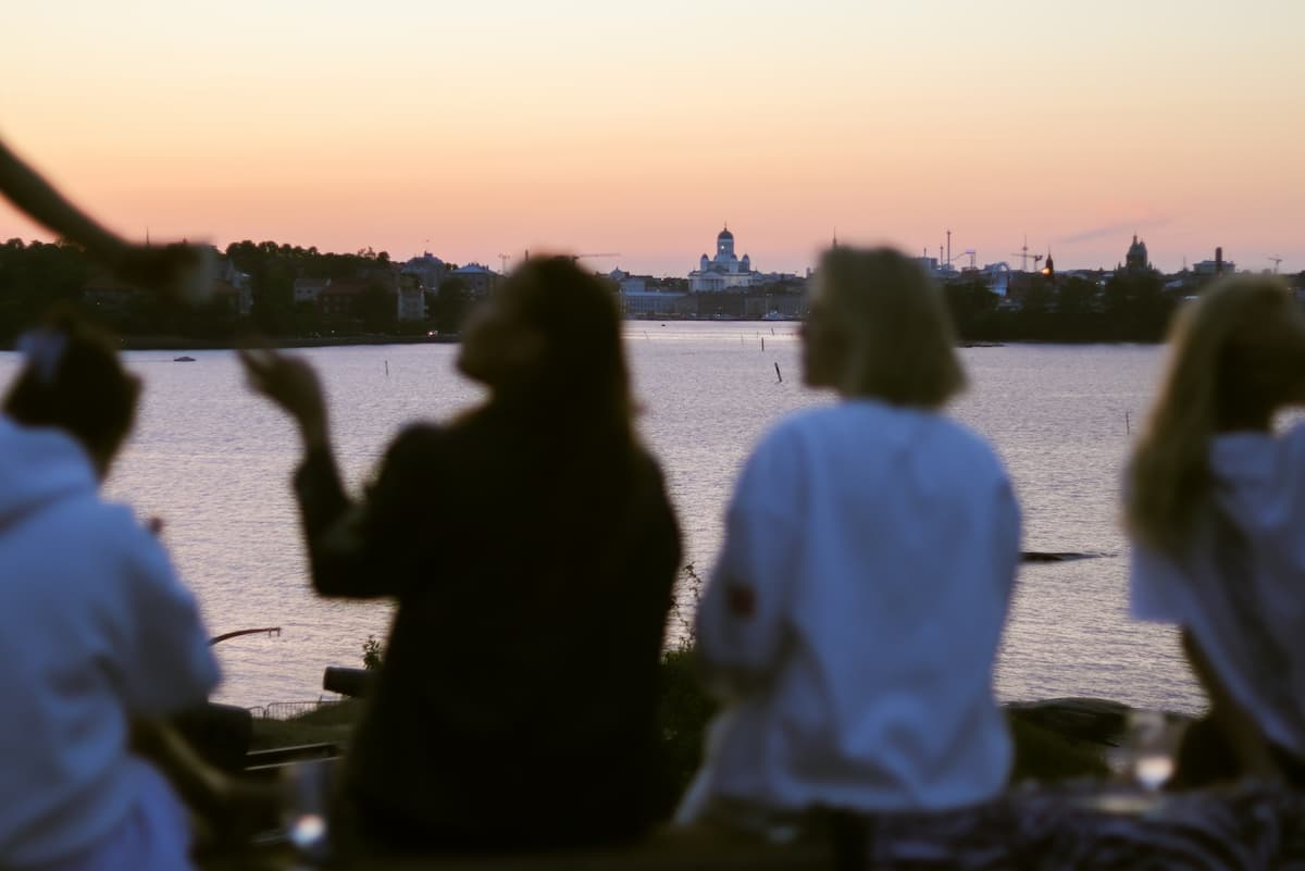 Nuoria henkilöitä istuu iltahämärässä meren rannalla.